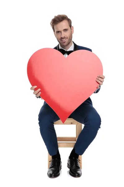 Sitzender stilvoller Mann hält ein großes rotes Herz in den Händen — Stockfoto