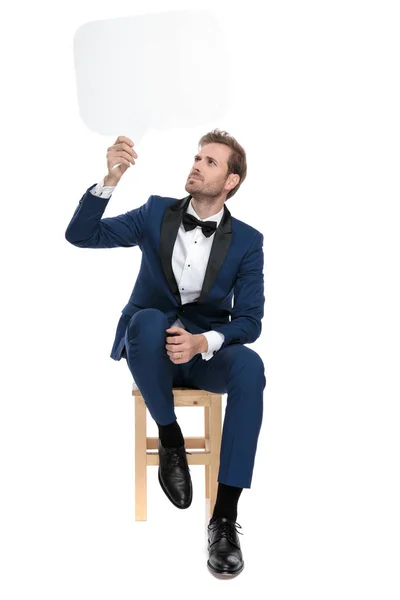 Sentado asombrado hombre sostiene la burbuja de chat en el aire — Foto de Stock