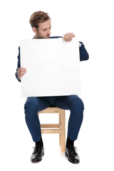 Ülő óvatos ember, aki egy üres tábla a kezében — Stock Fotó