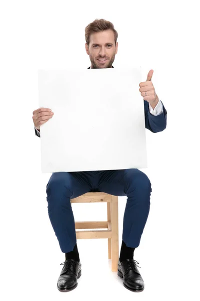 Współczesny człowiek pokazuje gest ok trzymając pustej planszy w pozycji siedzącej — Zdjęcie stockowe