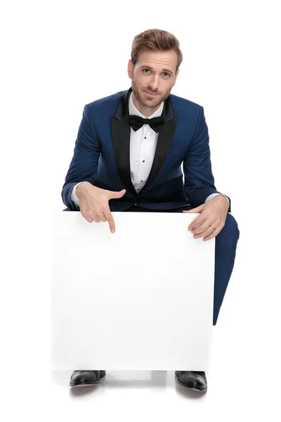Seated elegant man pointing his finger down to blank paper billb — Stock Photo, Image