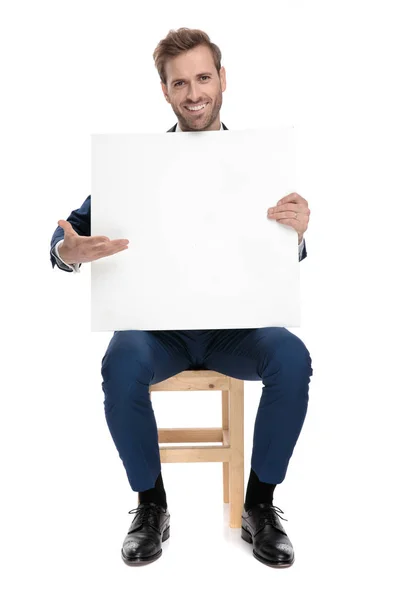 Sitzend sexy Mann in blauem Kostüm präsentiert eine leere Plakatwand — Stockfoto
