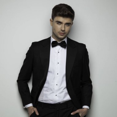 Siyah smokinli genç adam ceplerinde el ele tutuşuyor.