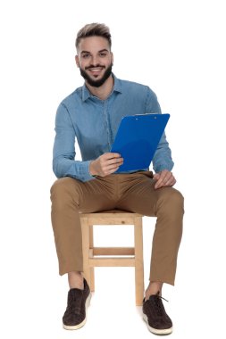 Genç adam elinde panoyla tahta sandalyede oturuyor.