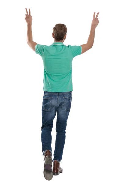 Mladý muž kráčející zpět s rukama nad hlavou ukazující V znamení — Stock fotografie