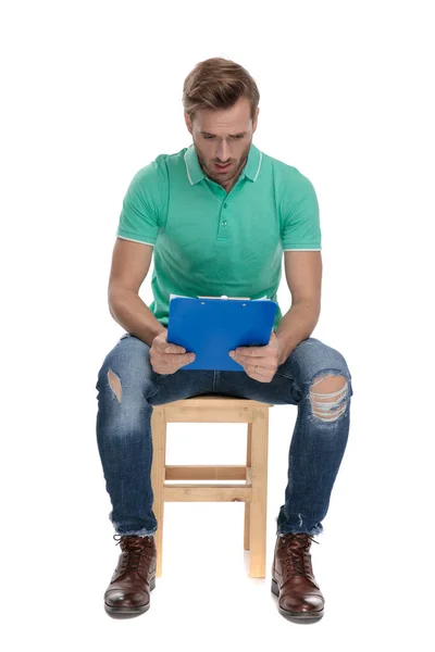 Καθισμένος έκπληκτος τύπος με πράσινο Polo πουκάμισο κοιτάζοντας το σημειωματάριο — Φωτογραφία Αρχείου