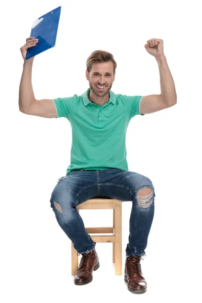 Seated sexy man celebrates with clipboard up in the air — стоковое фото