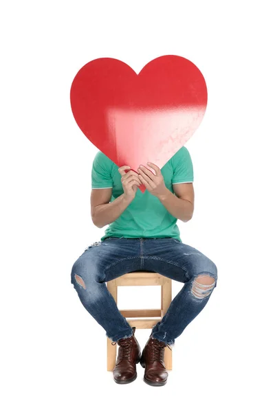 Sentado escondiendo su rostro detrás de un gran corazón rojo — Foto de Stock