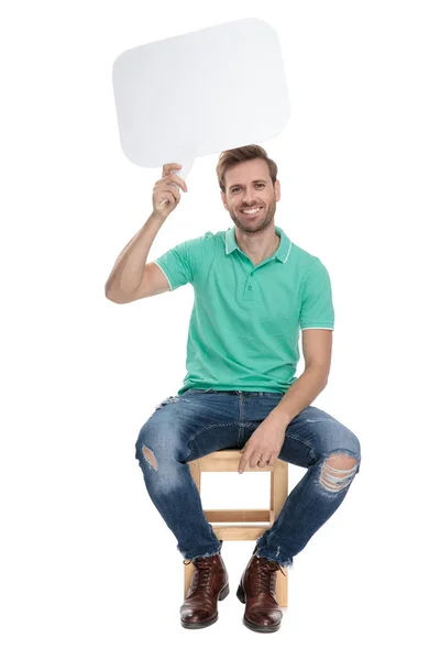 Oturmuş rahat adam boş bir konuşma balonu tutar — Stok fotoğraf