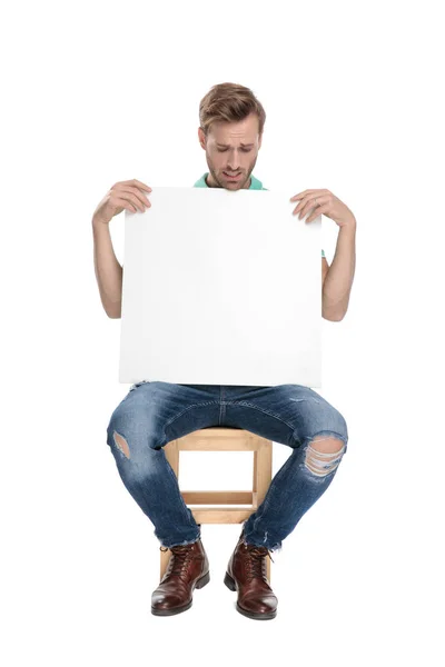 Сидящий обеспокоенный мужчина с пустым билбордом в руках — стоковое фото