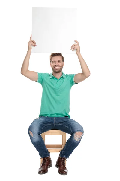 Oturmuş rahat adam havada karton reklam panosu tutar — Stok fotoğraf