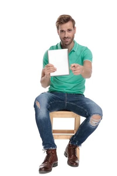 Sitzender glücklicher Mann zeigt mit dem Finger auf Kameraposter in der Hand — Stockfoto