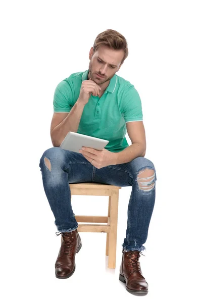 Siedzący młody facet myśląc z tabletem w ręku — Zdjęcie stockowe