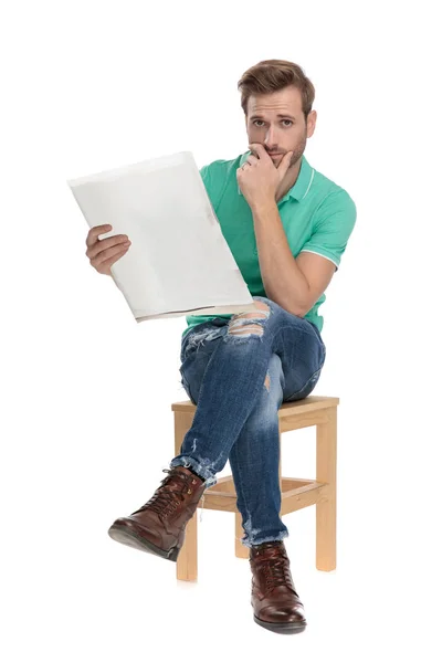 Sentado preocupado chico leyendo malas noticias con la mano en la barbilla —  Fotos de Stock
