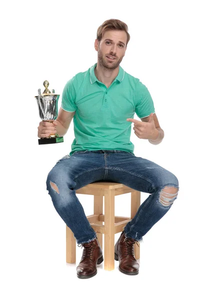 Sentado chico moderno señalando con el dedo a la copa de trofeo —  Fotos de Stock