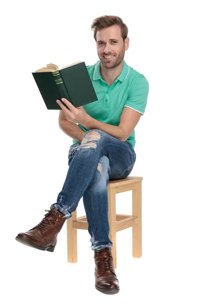 Sentado homem feliz segurando livro na mão com as pernas cruzadas — Fotografia de Stock