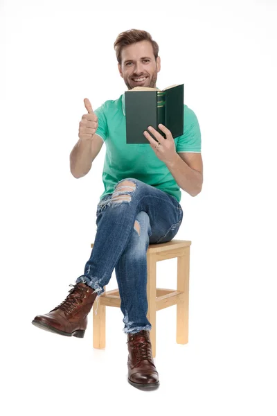 Sitzender cooler Mann zeigt ok Geste mit Buch in der Hand — Stockfoto