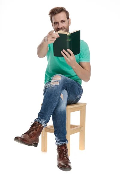 카메라에 자신의 손가락을 가리키는 손에 책을 가진 남자 — 스톡 사진