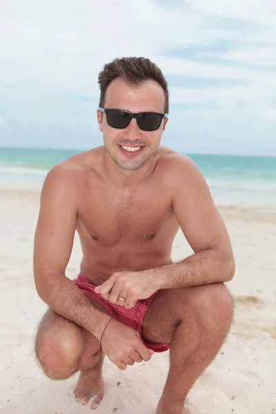 smiling crouched man standing on the beach