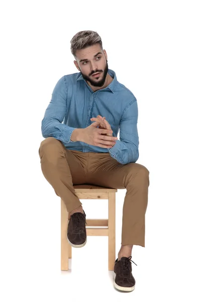 Sitzender bezauberter Mann schaut weg, während er sich die Handflächen reibt — Stockfoto