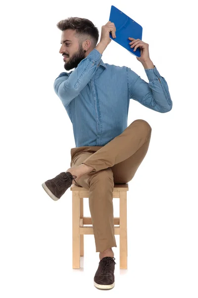 Modemann schlägt mit Klemmbrett zusammen, während er mit überkreuzten Beinen sitzt — Stockfoto