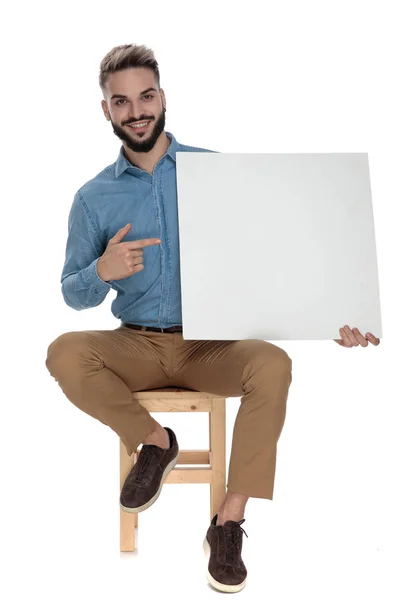 Siedzący dumny człowiek wskazując palcem puste Billboard — Zdjęcie stockowe