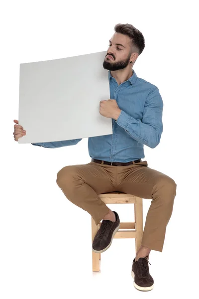 Hombre arrogante sentado recomendando una cartelera en blanco — Foto de Stock