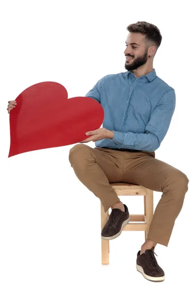 Sentado homem romântico em camisa jeans azul oferece coração vermelho — Fotografia de Stock