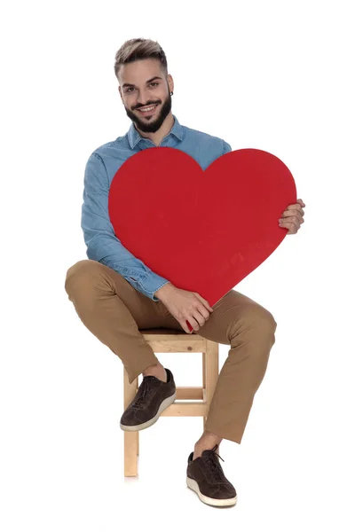 Sentado moda homem detém grande coração vermelho em suas mãos — Fotografia de Stock