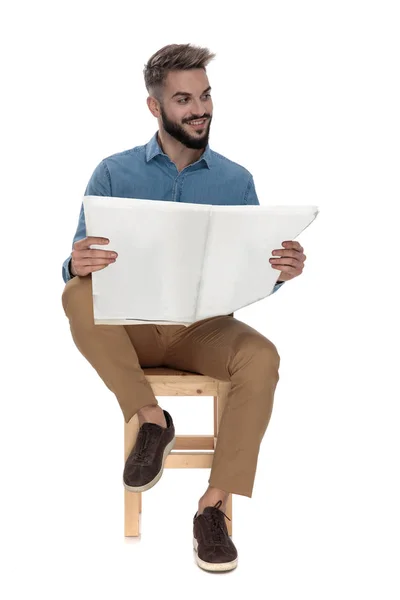 Homem moderno sentado com jornal nas mãos enquanto olha para longe — Fotografia de Stock
