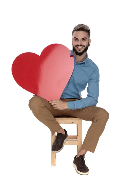 Καθισμένος όμορφος άνθρωπος κρατώντας μια κόκκινη σχήμα καρδιά στο χέρι — Φωτογραφία Αρχείου