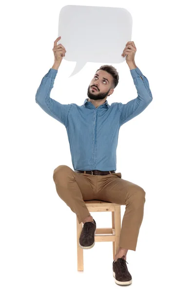 Sentado homem moderno segurando sinal de mensagem em branco enquanto olha para cima — Fotografia de Stock