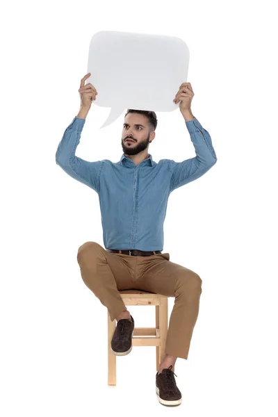 Hombre sin afeitar sentado y sosteniendo un signo de mensaje en blanco — Foto de Stock