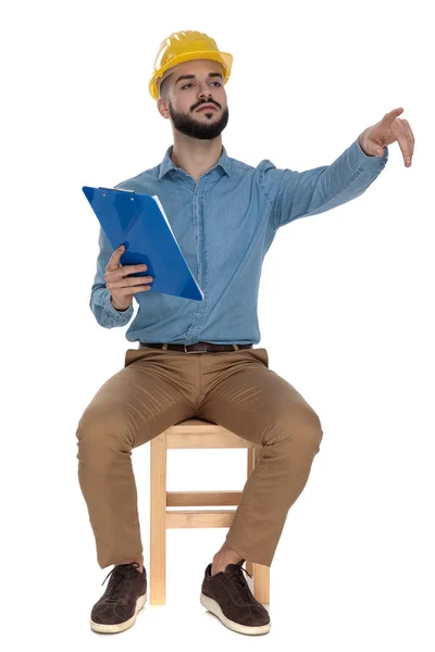 Ingeniero arrogante sentado señalando con el dedo mientras sostiene el portapapeles — Foto de Stock