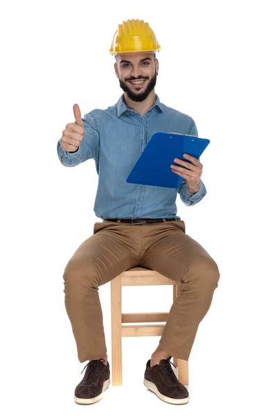 Oturmuş mutlu mühendis bir clipboa tutarken ok jest gösteren — Stok fotoğraf