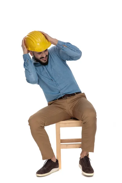 Scared man sitting with hands on yellow helmet — Stock Photo, Image