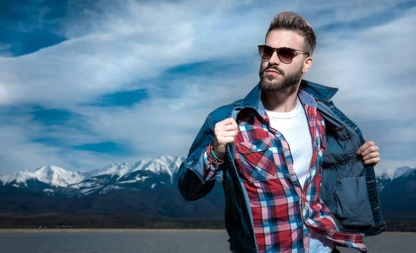 Hombre con gafas de sol tira del cuello de su chaqueta y mira hacia otro lado —  Fotos de Stock