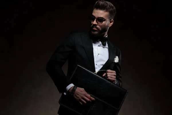 Sexy junger eleganter Mann im Smoking hält und öffnet Aktentasche — Stockfoto