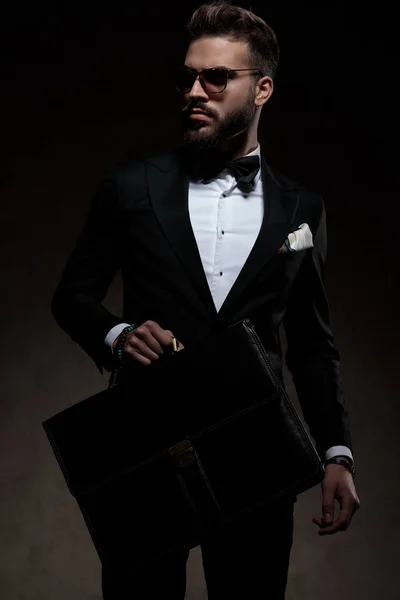 Elegant man in tuxedo holding a briefcase and looks away — Stock Photo, Image