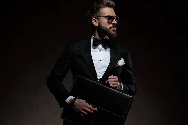 Cool guy in Tuxedo, bowtie en zonnebril houdt koffer — Stockfoto