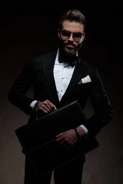 Dramatický elegantní muž v smokingu a sluneční brýle má kufřík — Stock fotografie
