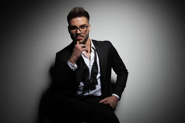 Handsome young man in black tuxedo holding hand on chin — Stock Photo, Image