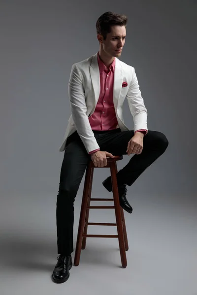 Sitzender Geschäftsmann im Anzug, der mit Arm am Bein wegschaut — Stockfoto