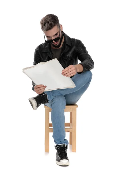 Man sitter på stol med benen korsade läsning tidningen — Stockfoto