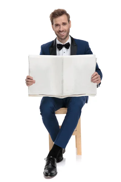 Sedící sexy muž v modrém obleku s novinami v ruce — Stock fotografie
