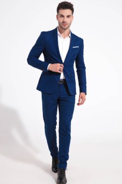 Kendine güvenen adam öne doğru yürüyor ve ceketini ayarlıyor.