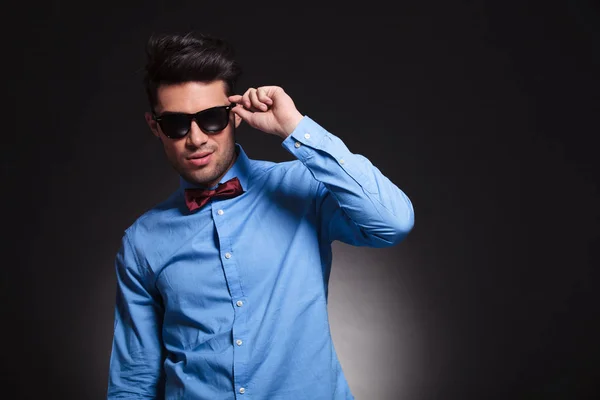 Charming young male standing and fixing his sunglasses — Stock Photo, Image