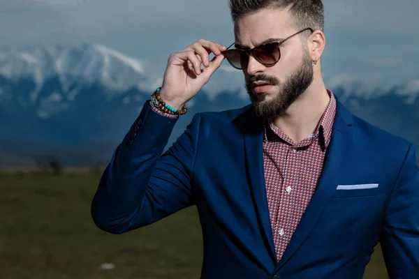 Jeune homme mystifié sur le point d'enlever ses lunettes de soleil — Photo