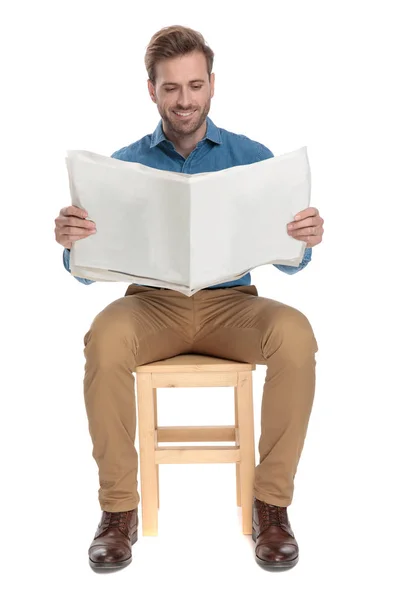 Positive guy holding and reading a newspaper while smiling — Stock Photo, Image