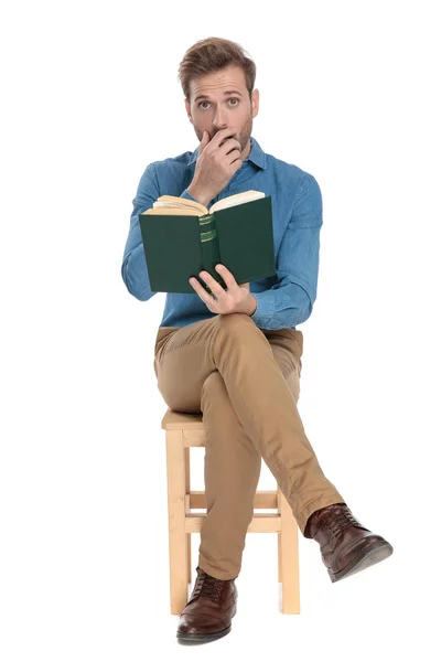 Verbaasd jonge man zitten en houden van een boek — Stockfoto